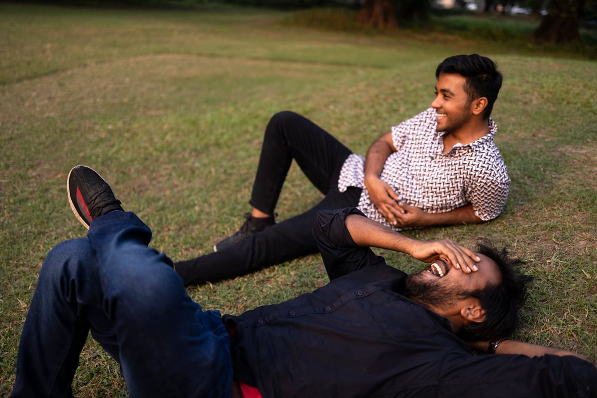 Two Friends Relaxing And Interacting Lying On Grass Ground