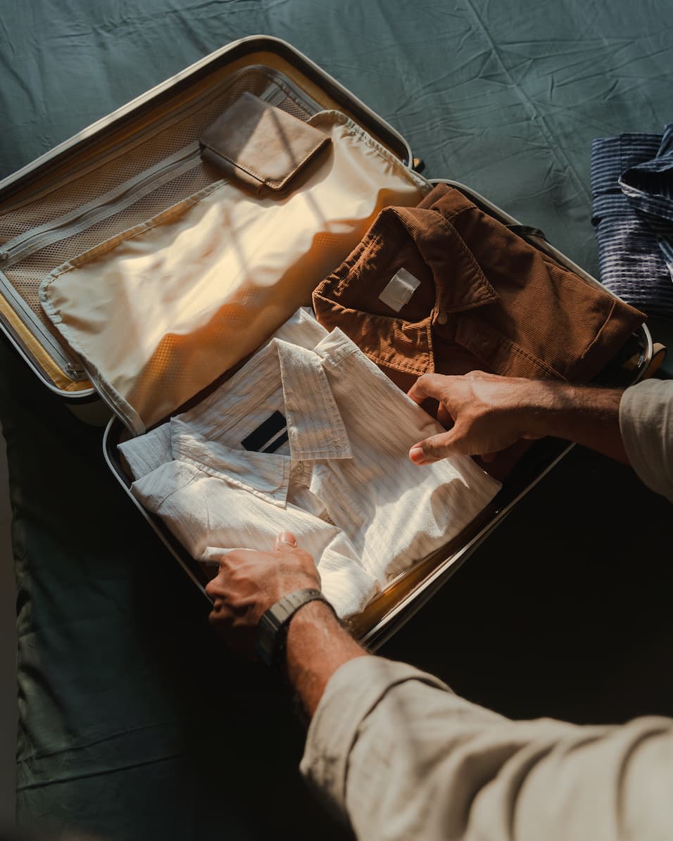 Close-up of a traveller’s hands packing neatly folded shirts and essentials into a suitcase, preparing for a well-organized journey.