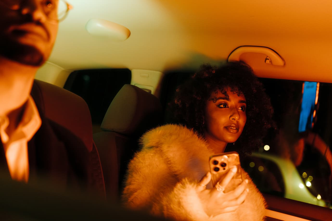 Portrait with cinematic light of young woman with afro hair inside car at night, holding a phone