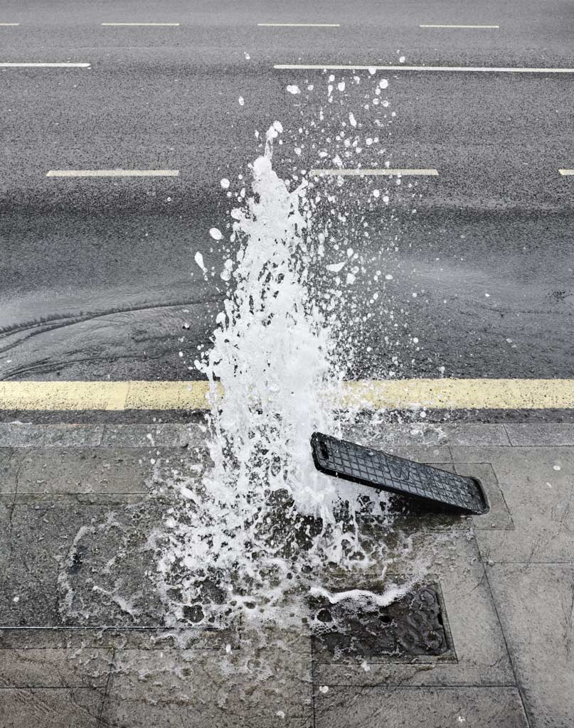 A burst water pipe by the side of an empty road