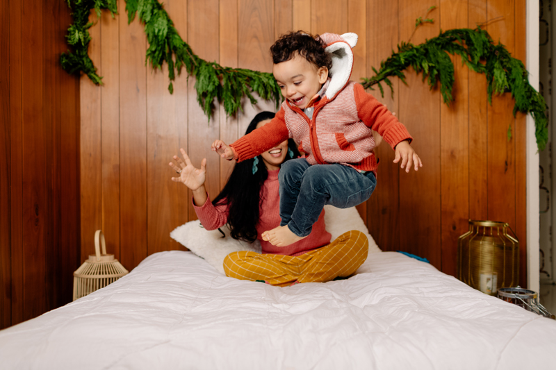 Playful Kid Jumping On Bed With Mother During Christmas Time