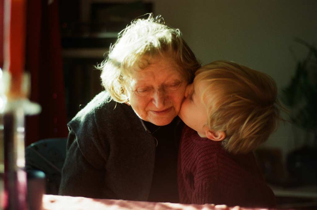 a film shot of a child grandchild kissing his old smiling grandmother, natural sunlight, indoor, during christmas lunch
