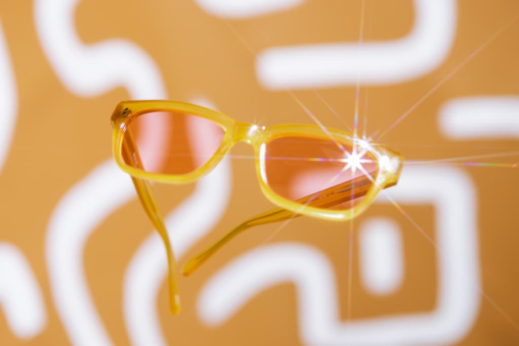 Orange sunglasses front, with pink lenses floating with orange and white background