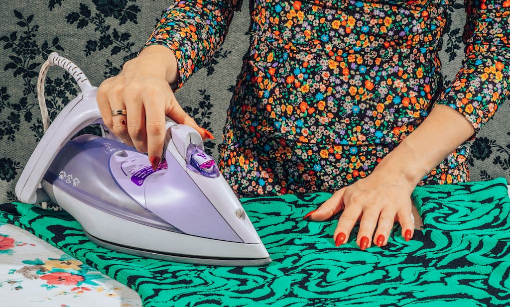 Female hands pressing iron while ironing clothes.