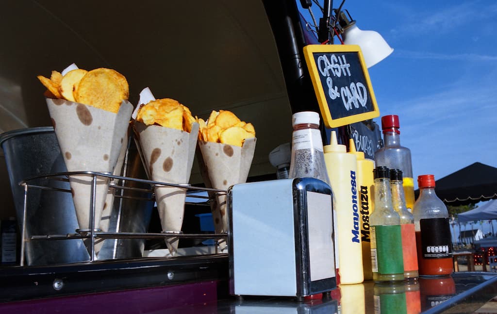 A street food stand offers chips in paper cones with various condiments available, ready for customers to enjoy on the go.